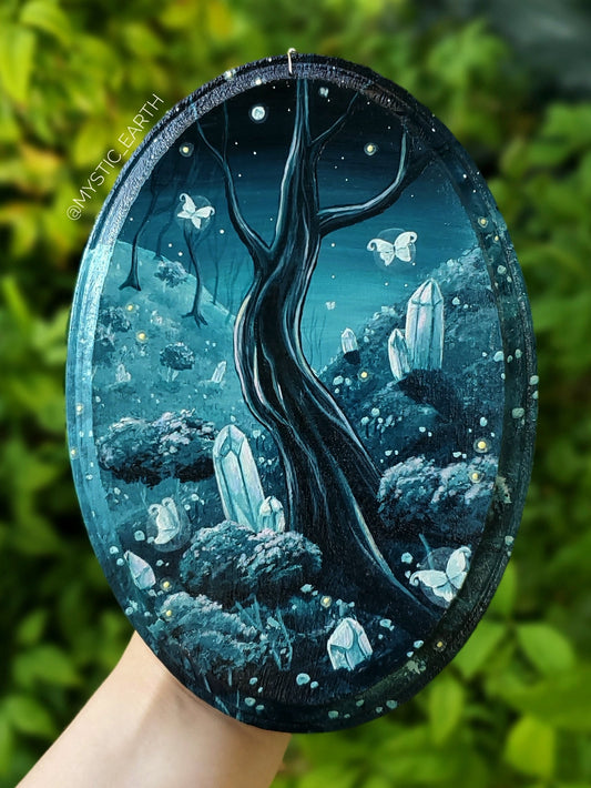 Acrylic painting on oval shaped wood, in monochrome teal blue. Depicts forested hills in the nightime with bare trees, crystals growing in the grass, bushes, and flowers. Fairies and fireflies float in the sky