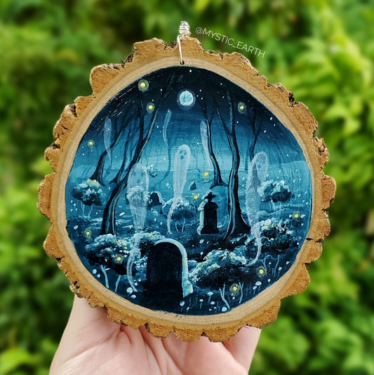 A 4" painting done on a wood slice. The natural edge of the wood is showing. The painting depicts a forest cemetery with 6 ghosts, fireflies, and a full moon. Done in teal blue monochrome